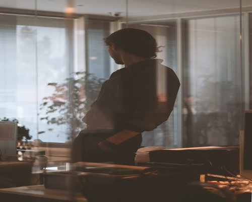 A person standing next to their office desk looking out a window